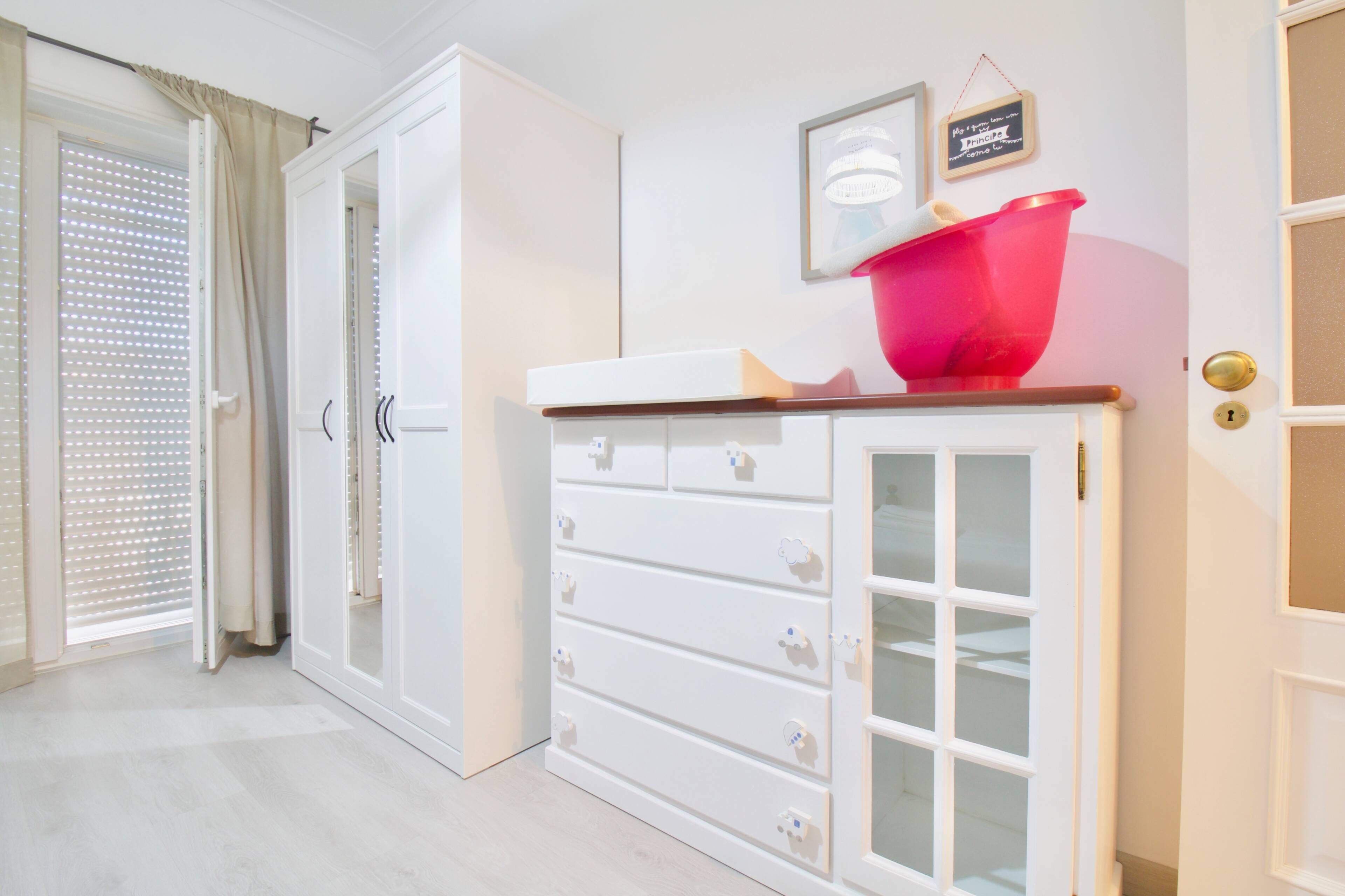 Une pièce avec une armoire blanche, un bol rouge posé sur le dessus, et une porte dotée d’une poignée en laiton.
