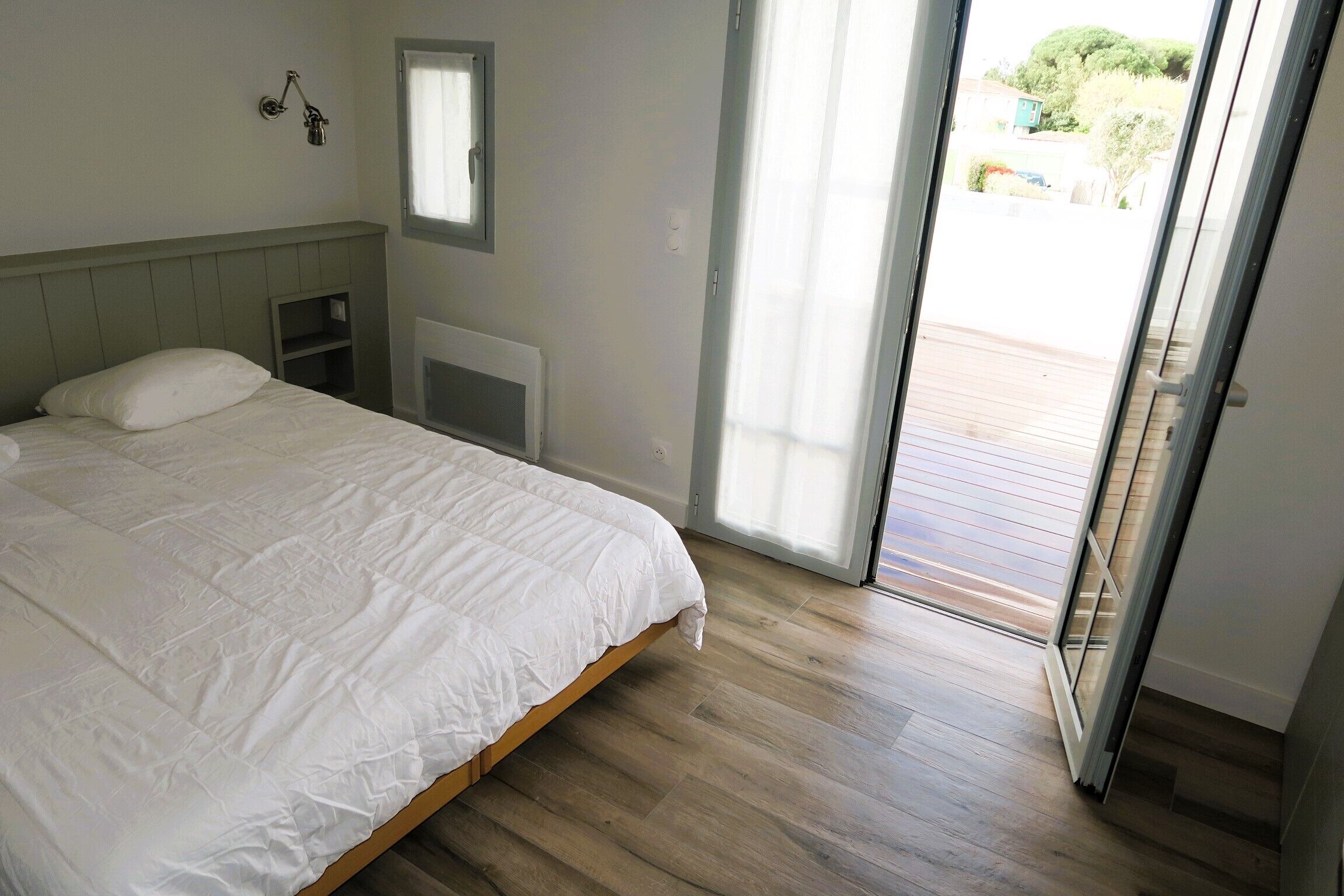 A bedroom with a bed, a nightstand, a window, and a door leading to an outdoor deck.