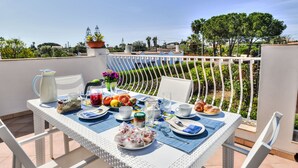 A balcony table set with plates, cups, and a pitcher, overlooking a garden and buildings. - MareLuna by Interhome (Fontane Bianche)