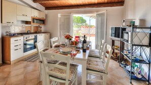 A kitchen with wooden ceiling beams, white cabinets, a dining table with chairs, and a view of the outside. - MareLuna by Interhome (Fontane Bianche)