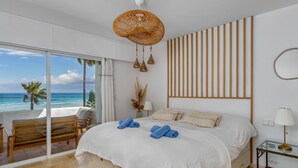 A bedroom with a large bed, a view of the ocean, a wooden bench, and a glass table with a lamp. - Apartment Ayla by Interhome (Casares)