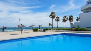 A swimming pool with a clear blue water, surrounded by palm trees and a beach view. - Apartment Ayla by Interhome (Casares)