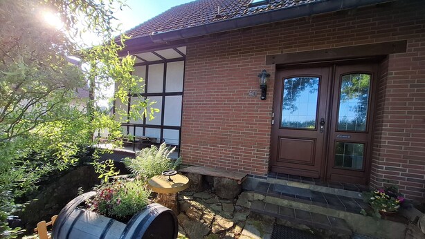 A brick house with a traditional design, a front door, and a small outdoor seating area with a barrel and plants.