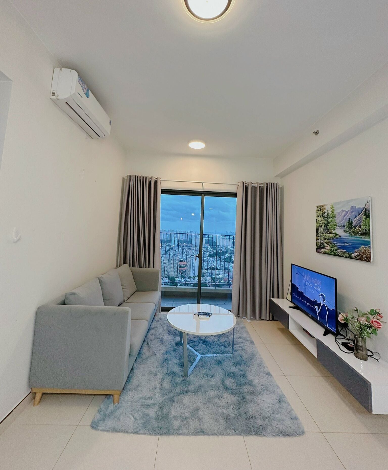 A modern living room with a grey sofa, a round coffee table, a flat-screen TV, and a painting on the wall.