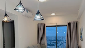 Un salon moderne avec un coin repas, un canapé gris et une vue sur la ville grâce à de grandes fenêtres.