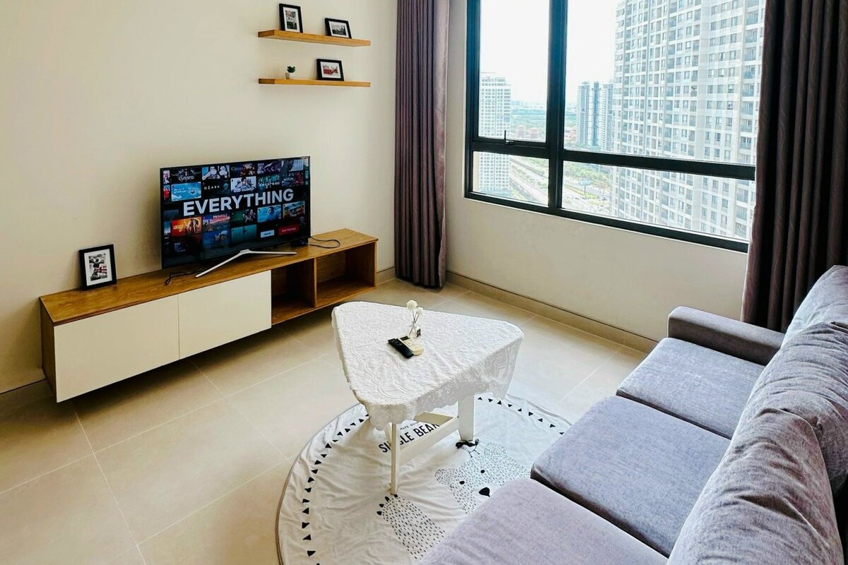 Een moderne woonkamer met een grote televisie, een bank, een bijzettafeltje en een raam met gordijnen.