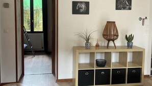A living room with a wooden floor, a sofa, a console table with decorative items, and a view through an open door to a balcony. - Superbe Appartement Neuf Face au Château - 2 ch / 5 Pers - Netflix Canal+ - Wifi (Sedan)