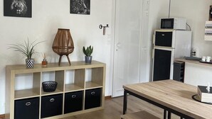 A modern kitchen with wooden beams, a wooden table, and a bench. There are two black refrigerators, a microwave, and a coffee machine on the counter. - Superbe Appartement Neuf Face au Château - 2 ch / 5 Pers - Netflix Canal+ - Wifi (Sedan)