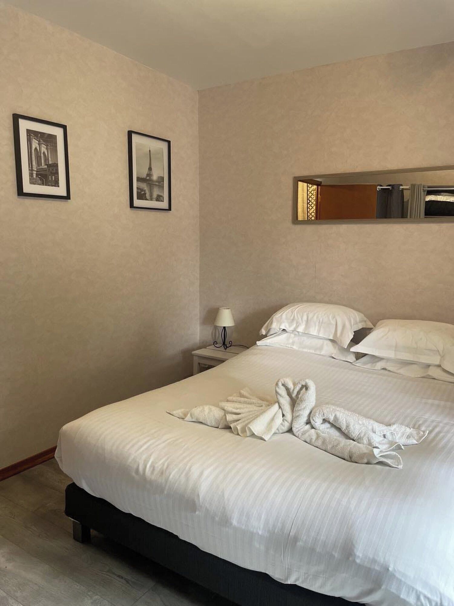 Una habitación de hotel con una cama bien hecha, una mesita de noche con lámpara y dos cuadros en la pared.