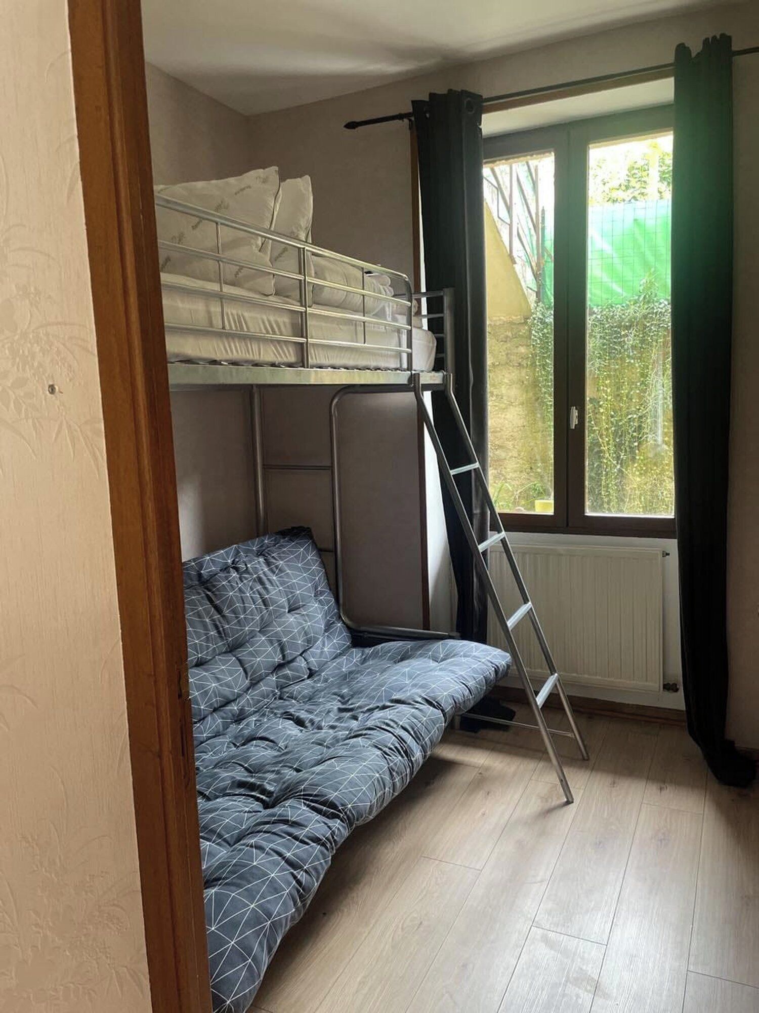 Una camera compatta con un letto a castello, un letto singolo, una finestra con tende e un termosifone.