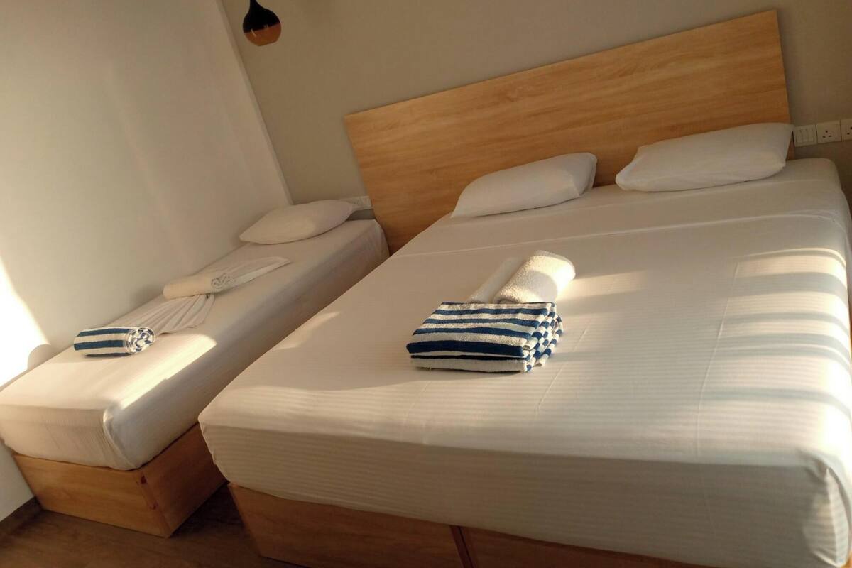 A hotel room with two single beds, each with a wooden headboard, white bedding, and a small bedside table with a lamp.