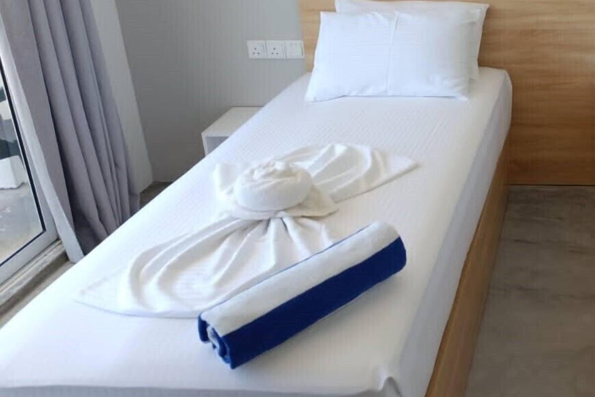 A hotel room with a wooden headboard, white bedding, a rolled towel, and a blue towel on the bed.