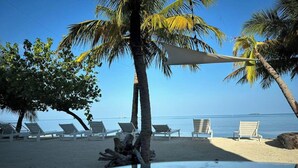 A beach with lounge chairs and a pool reflecting palm trees. - The Sunset Villa (Dhiffushi)