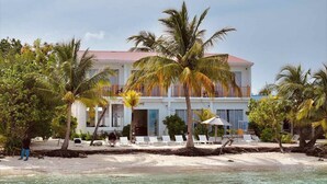 A beachfront hotel with a white facade, palm trees, and a sandy beach. - The Sunset Villa (Dhiffushi)
