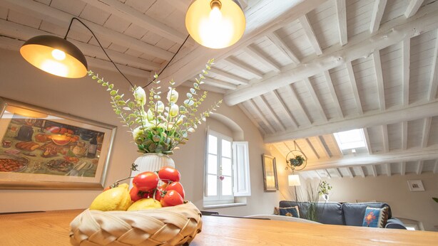Een eethoek met een houten tafel, een rieten mand met fruit, hangende pendellampen en een wit plafond met zichtbare balken.