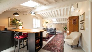 Een ruime woonkamer met een houten eettafel, een bank en een stoel. Er is een keuken met een zwart aanrecht en een rode stoel.