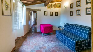 Un cuarto acogedor con piso de piedra, un sofá azul con estampado, una silla roja y un pasillo que conduce a otra habitación.