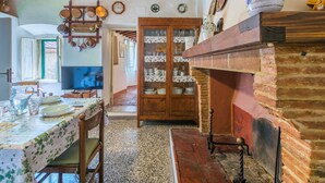 Una cocina rústica con vigas de madera a la vista, chimenea de ladrillo y comedor con una mesa lista para dos personas.