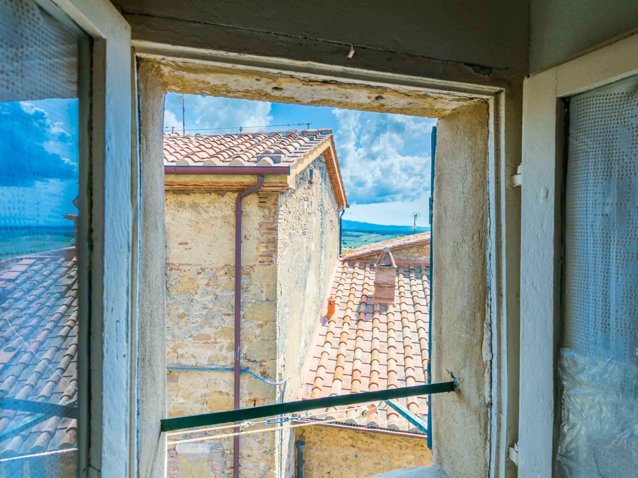 A view through a window of a building with a tiled roof and a stone wall.