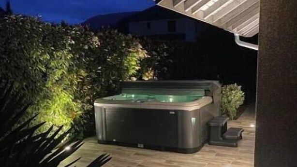 Un espace extérieur aménagé avec un jacuzzi et une terrasse en bois, le tout entouré de verdure.