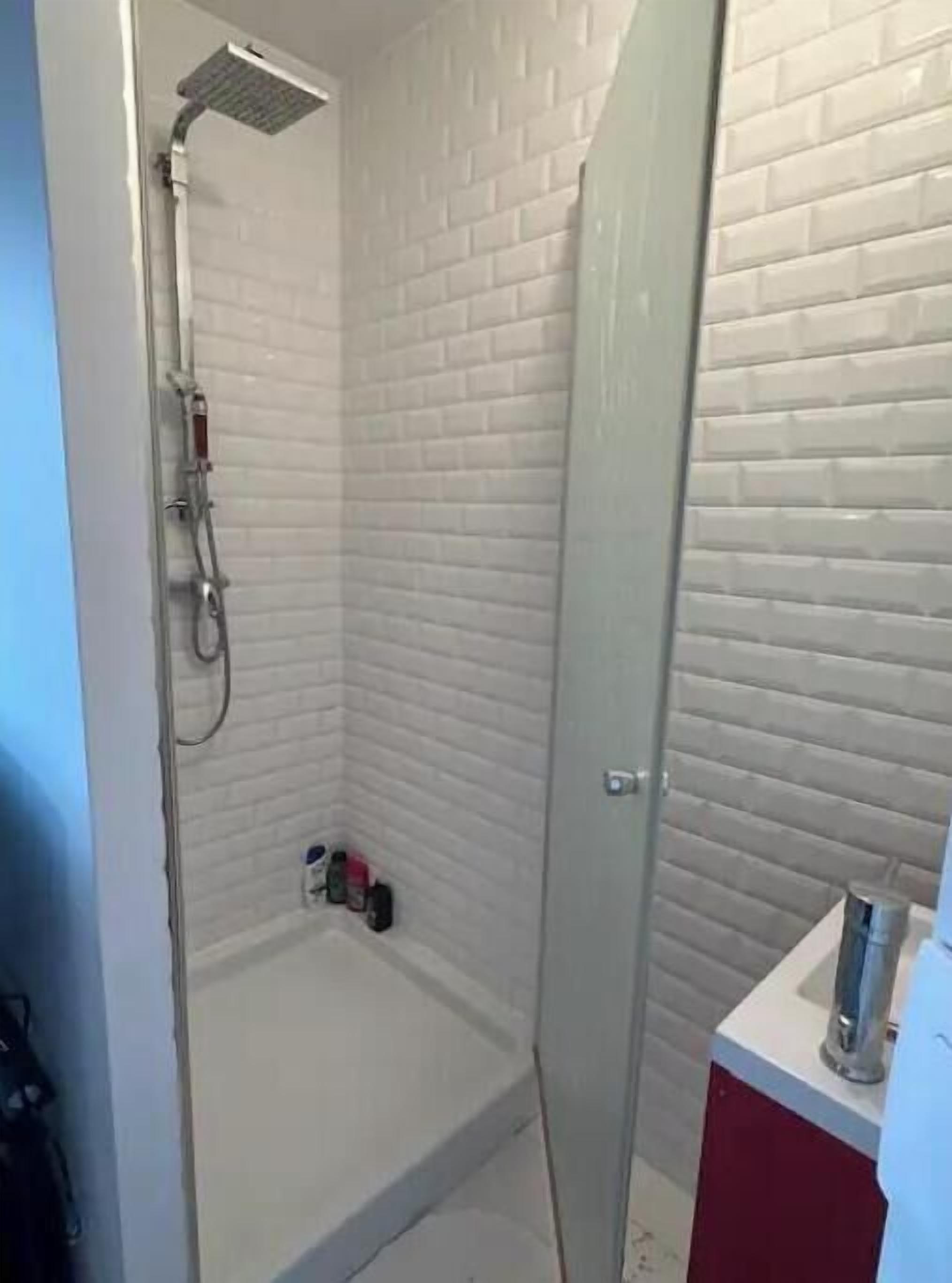 A small, enclosed shower area with white tiled walls and a glass door.