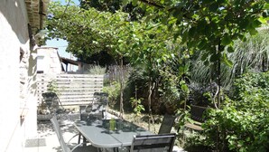 An outdoor dining area with a table and chairs, surrounded by lush greenery and a stone wall. - Propriété en pleine nature   (Beynes)