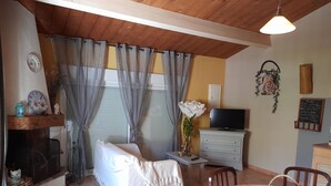 A cozy living room with a fireplace, a sofa, a TV, and a dining area with chairs and a table. - Propriété en pleine nature   (Beynes)