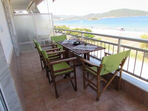 Ein Balkon mit Holztisch und -stühlen mit Blick auf Strand und Meer.