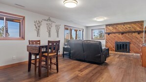 A spacious living area with a dining table and chairs, a black leather sofa, and a fireplace. - Pinedale Cabin Getaway (Rapid City)