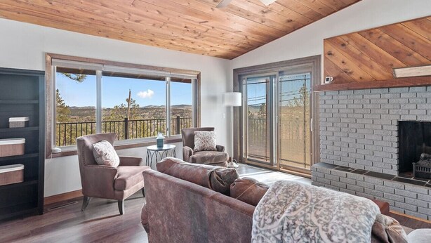 A spacious living room with a fireplace, large windows, and a high ceiling with wooden beams. - Pinedale Cabin Getaway (Rapid City)