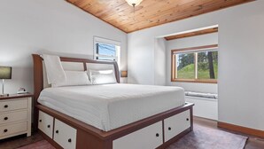 A bedroom with a wooden bed, white bedding, a nightstand, a lamp, and a window with a view of greenery. - Pinedale Cabin Getaway (Rapid City)
