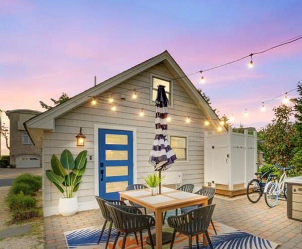 A cozy cottage with a blue door, a small porch with a table and chairs, and string lights. - Beach Daze|Beachfront Bungalow+HotTub+Beach Access (Sea Bright)