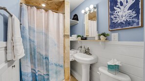 A bathroom with a shower curtain, a sink, a toilet, a mirror with lights, and a framed artwork on the wall. - Beach Daze|Beachfront Bungalow+HotTub+Beach Access (Sea Bright)