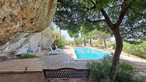 Un espace piscine comprenant un banc, des chaises longues et une grande formation rocheuse.