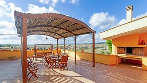 Une terrasse extérieure couverte, avec une table et des chaises, une balançoire et un four en briques.