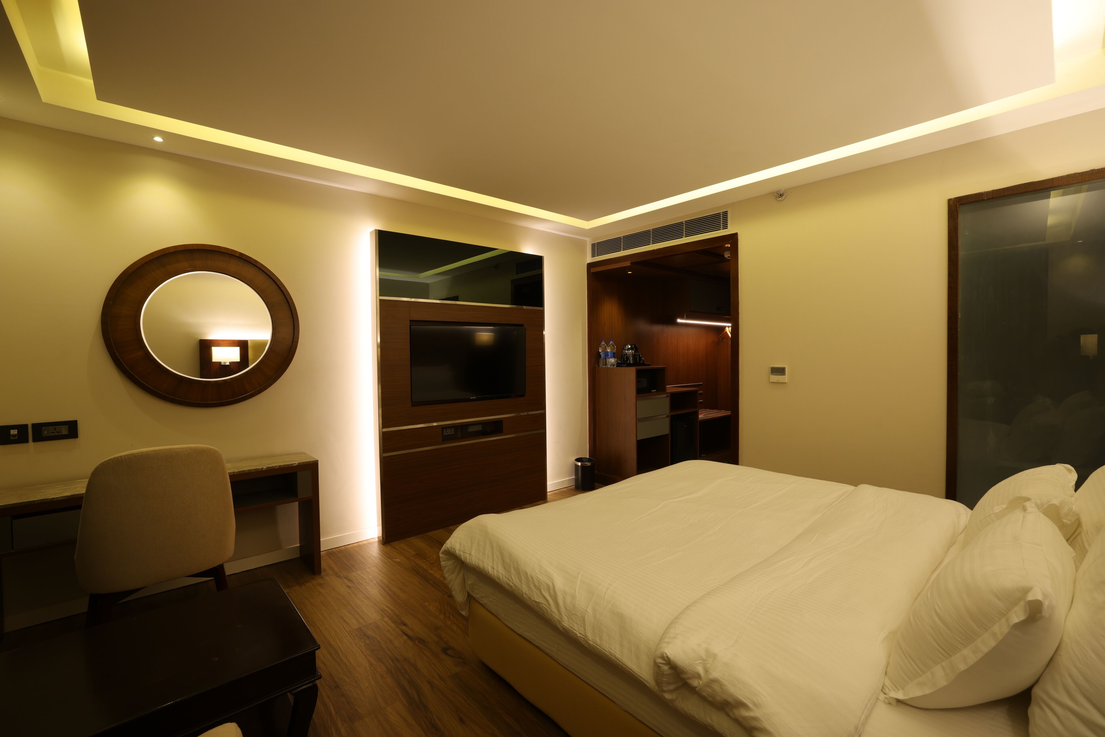 Habitación de hotel con cama, escritorio, silla, televisor, espejo y armario.