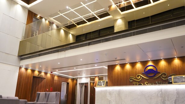 A hotel reception area with a marble counter, seating, and a wooden wall. - The Sea View (Mangaluru)