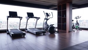A gym with treadmills, an elliptical, and a stationary bike, with a city view through large windows. - The Sea View (Mangaluru)