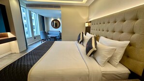 A hotel room with a large bed, a headboard, a bedside table, a chair, and a view of the outside through a window. - The Sea View (Mangaluru)