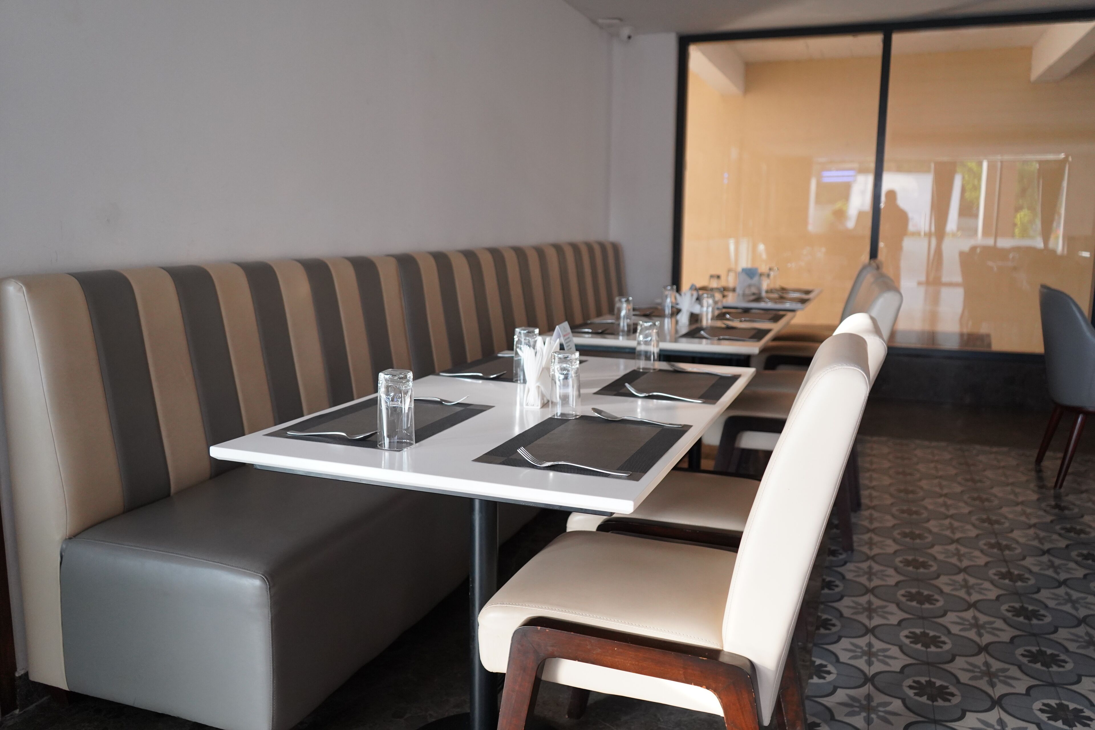 Un comedor con una mesa larga dispuesta para cuatro, un banco acolchado y un suelo estampado.