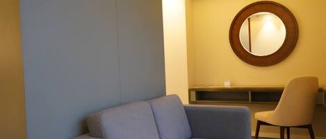 Una habitación moderna con un sofá gris, un espejo redondo y una silla color beige.