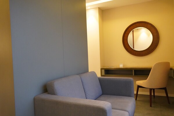 A modern room with a grey sofa, a round mirror, and a beige chair. - The Sea View (Mangaluru)