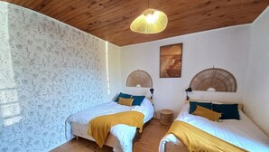 Habitació amb dos llits, terres de fusta, paper pintat amb dibuixos i un ventilador de sostre.