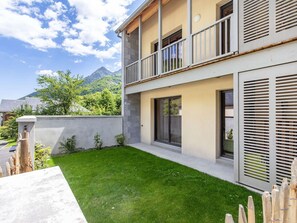 Una casa moderna de dos pisos con un balcón, un césped cuidado y una vista a la montaña al fondo.
