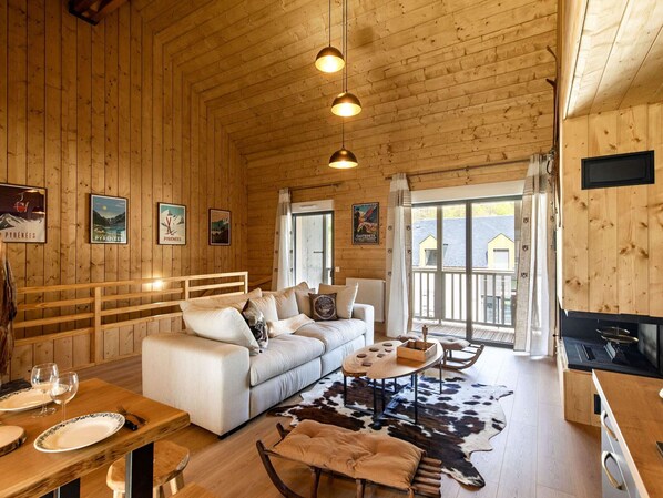 Interior acogedor de una cabaña con detalles de madera, un sofá, una mesa de comedor para dos personas y una zona de cocina.