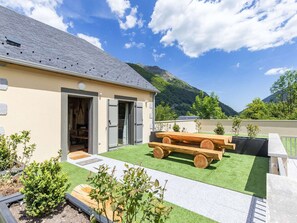 Un edificio con techo inclinado, un patio con césped artificial, bancos de madera y vistas a montañas.