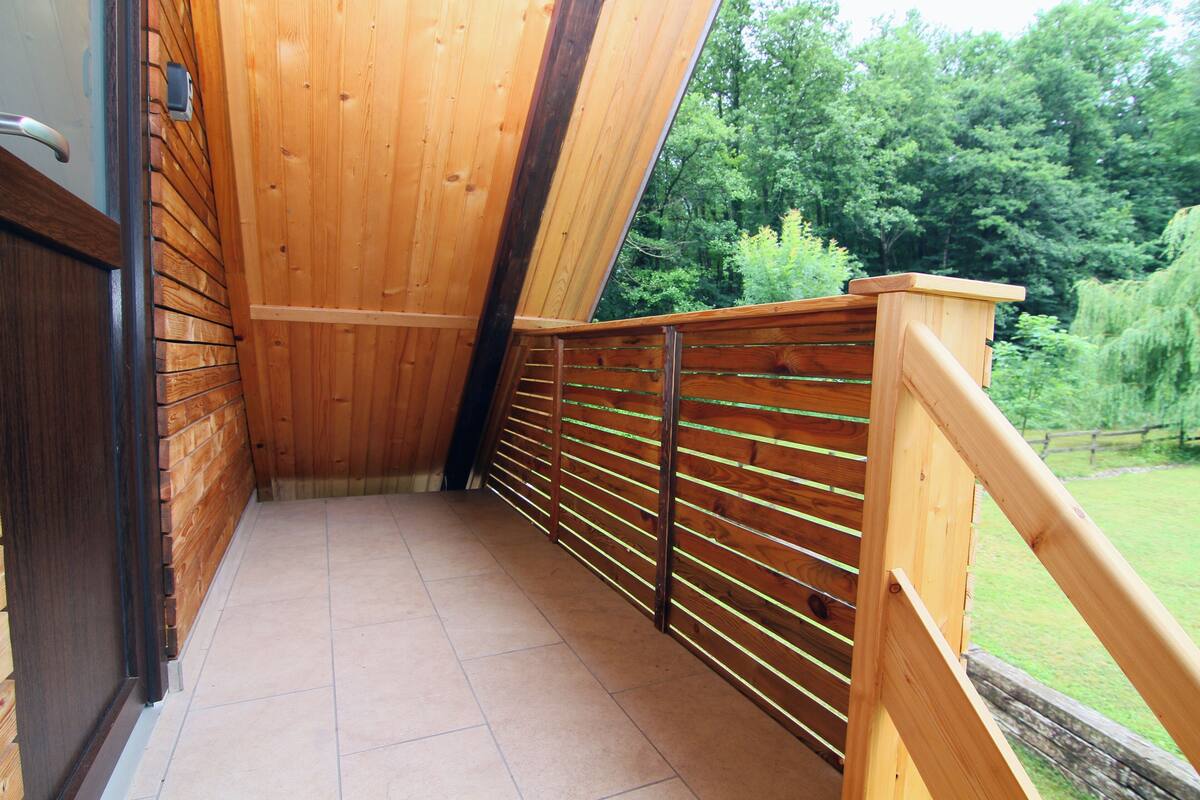 Ein Holzbalkon mit Metallgeländer, einem gefliesten Boden und Blick auf eine grüne Landschaft.