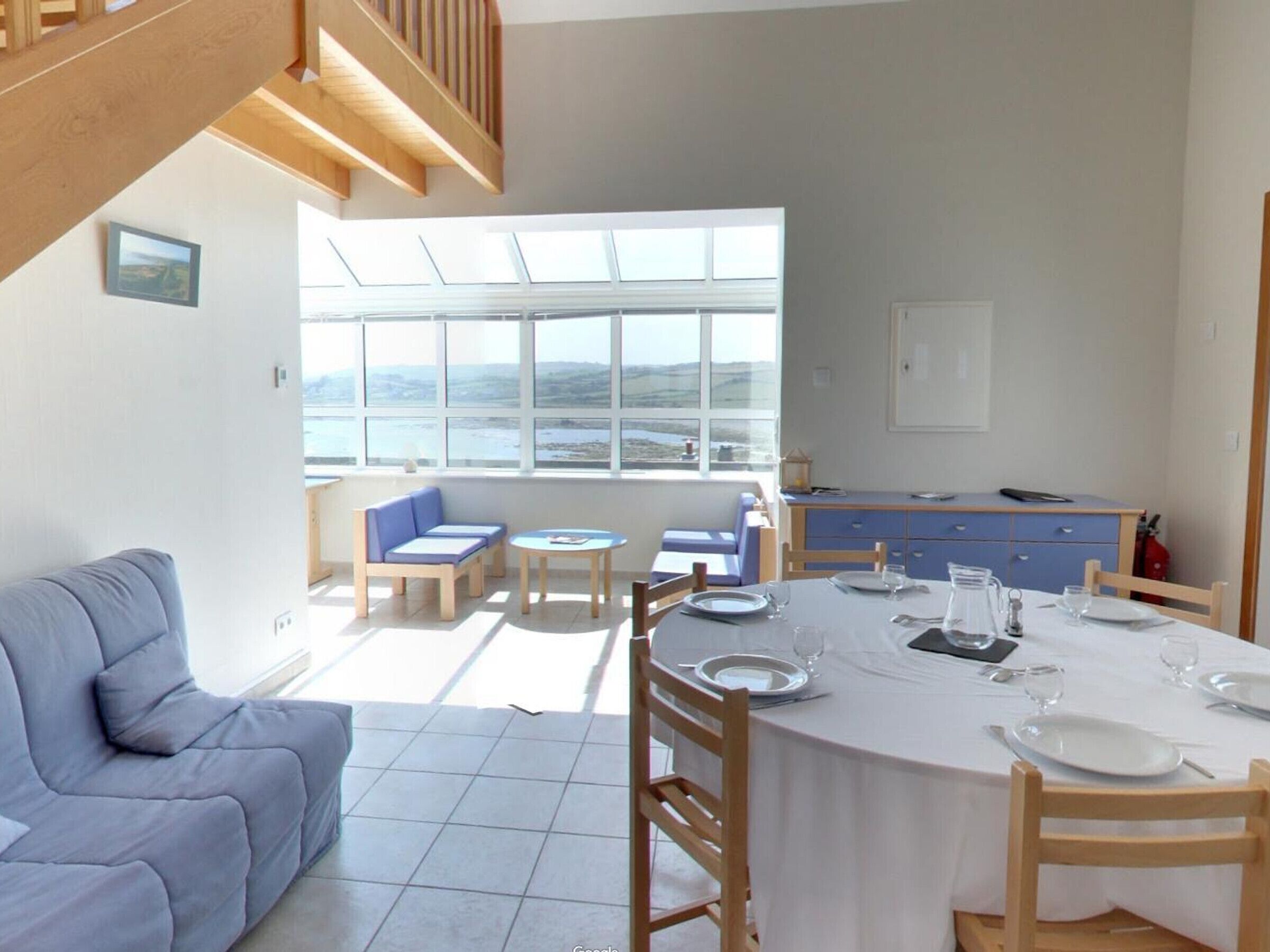 A dining area with a table set for four, a sofa, and a view of the sea through large windows.
