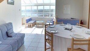 Un coin repas avec une table dressée pour quatre personnes, un canapé et une vue sur la mer grâce à de grandes fenêtres.
