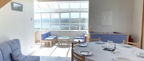 A dining area with a table set for four, a sofa, and a view of the sea through large windows.